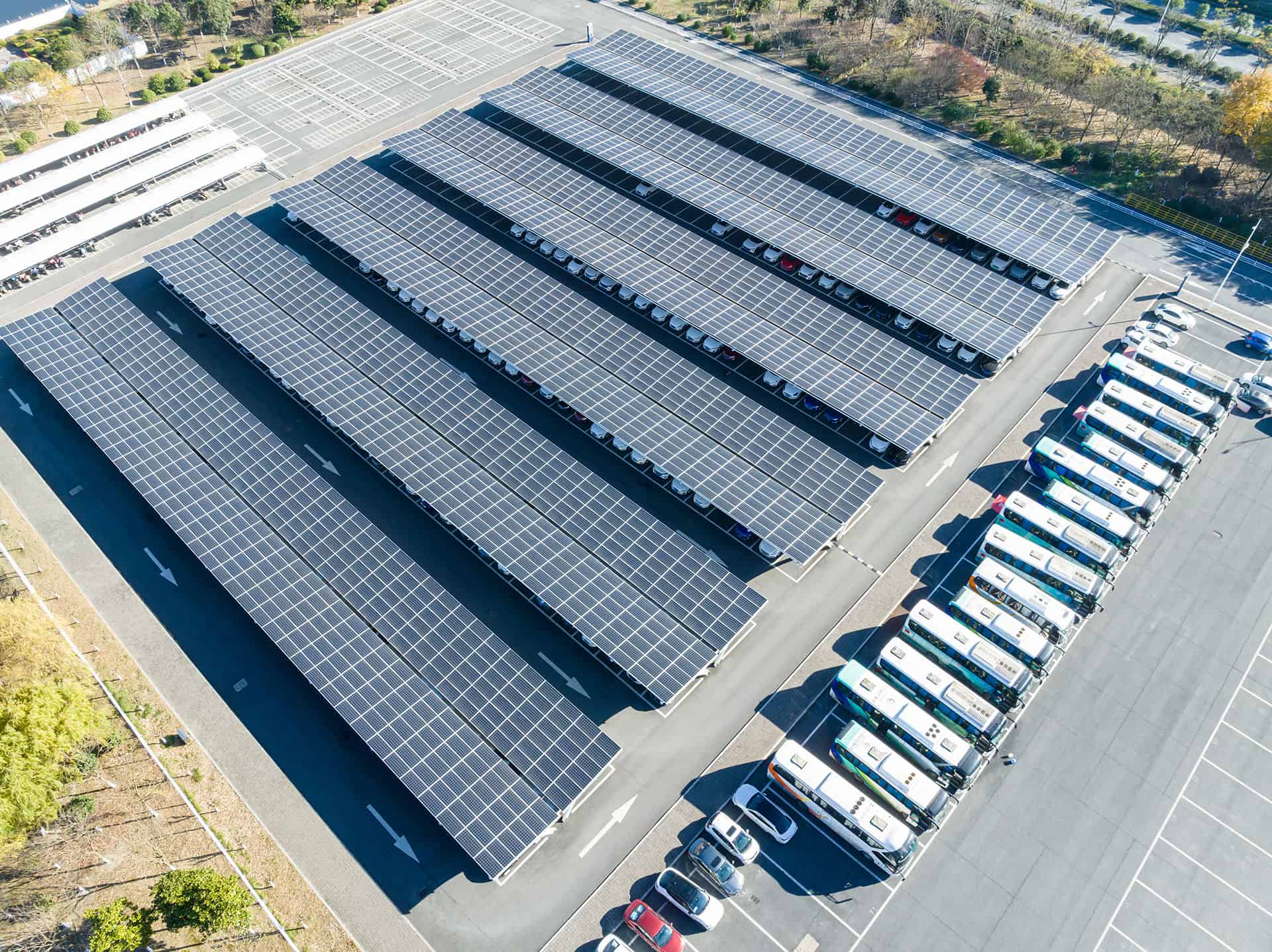 Großer Firmenparkplatz, der mit Solarpaneelen überdacht ist, aus der Vogelperspektive.