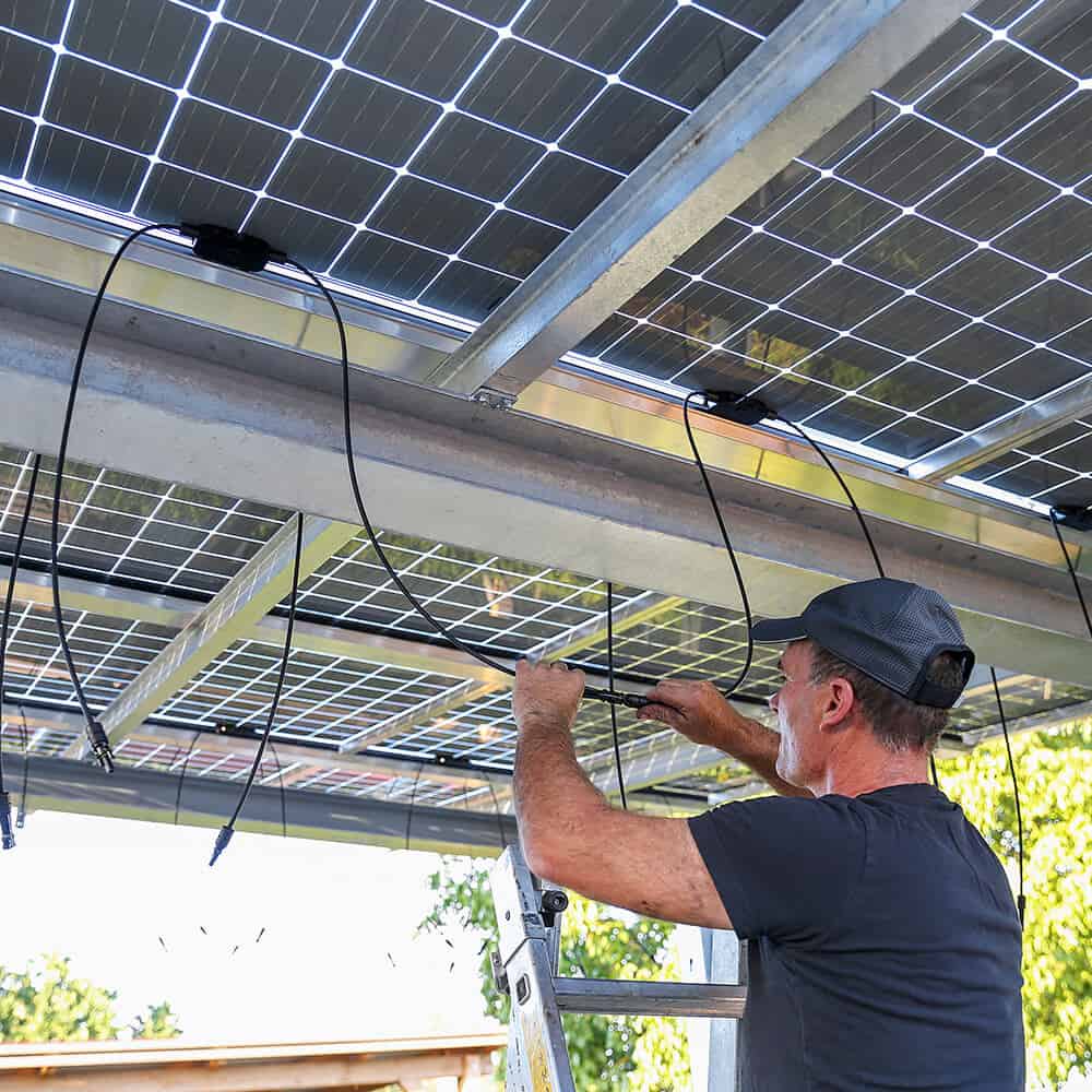 Photovoltaik-Überdachung, Mann steckt Solarmodule über Kopf zusammen