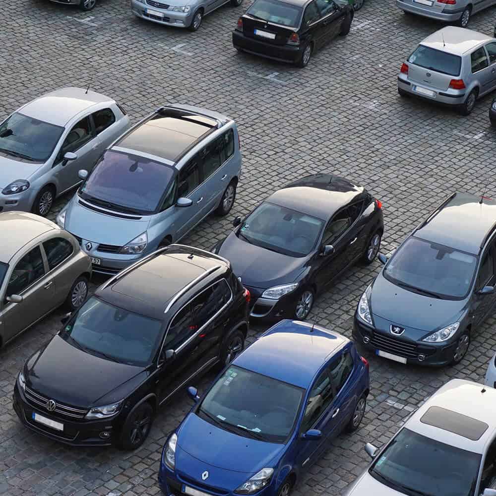 Eine gepflasterte Parkplatzfläche, voll mit Autos in dunklen Farben.
